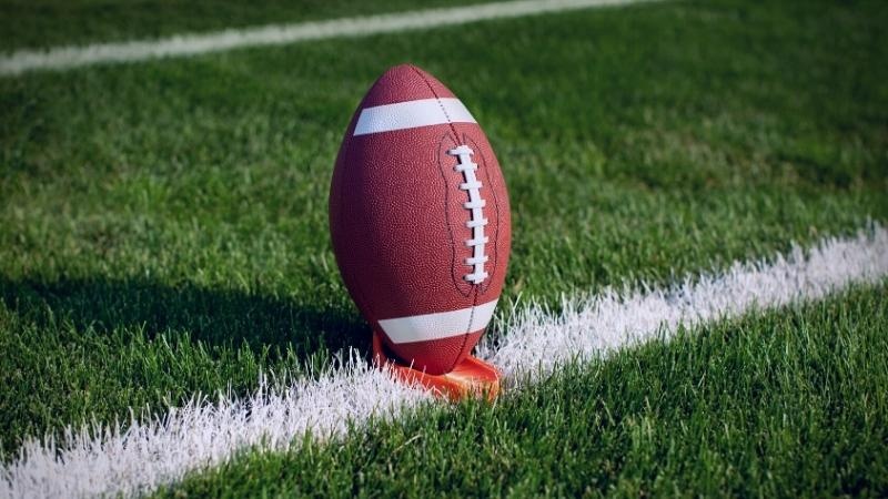 Football sitting on orange tee on the yard line of a green football field.